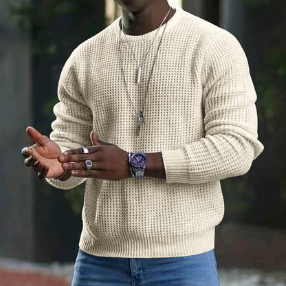 Mann in cremefarbenem Strickpullover, trägt silberne Halsketten und Armbanduhr, gestikuliert mit Händen. Mode, Herrenbekleidung, Accessoires.