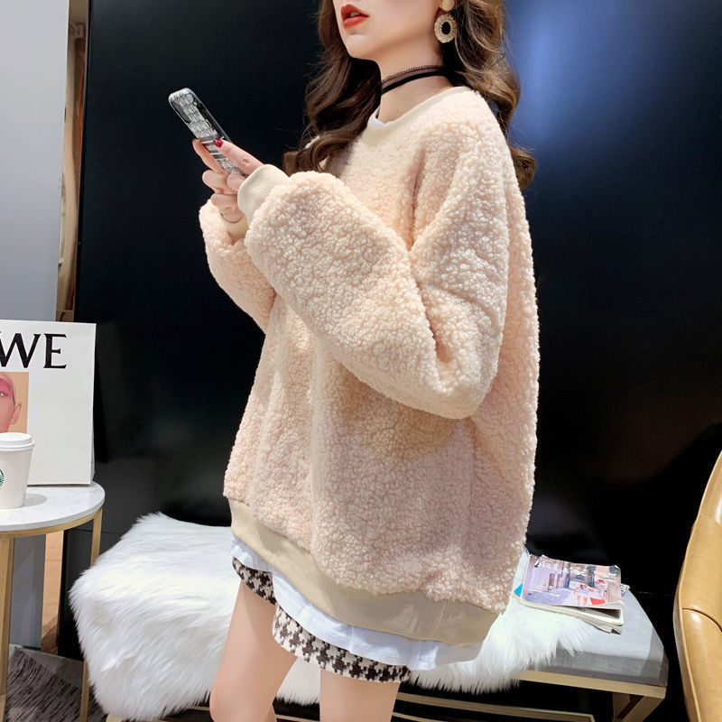 Frau in beigem Teddy-Fleece-Pullover, hält Smartphone, sitzt in modernem Café. Modetrend, Wintermode, gemütlicher Look, stilvolle Freizeitkleidung.