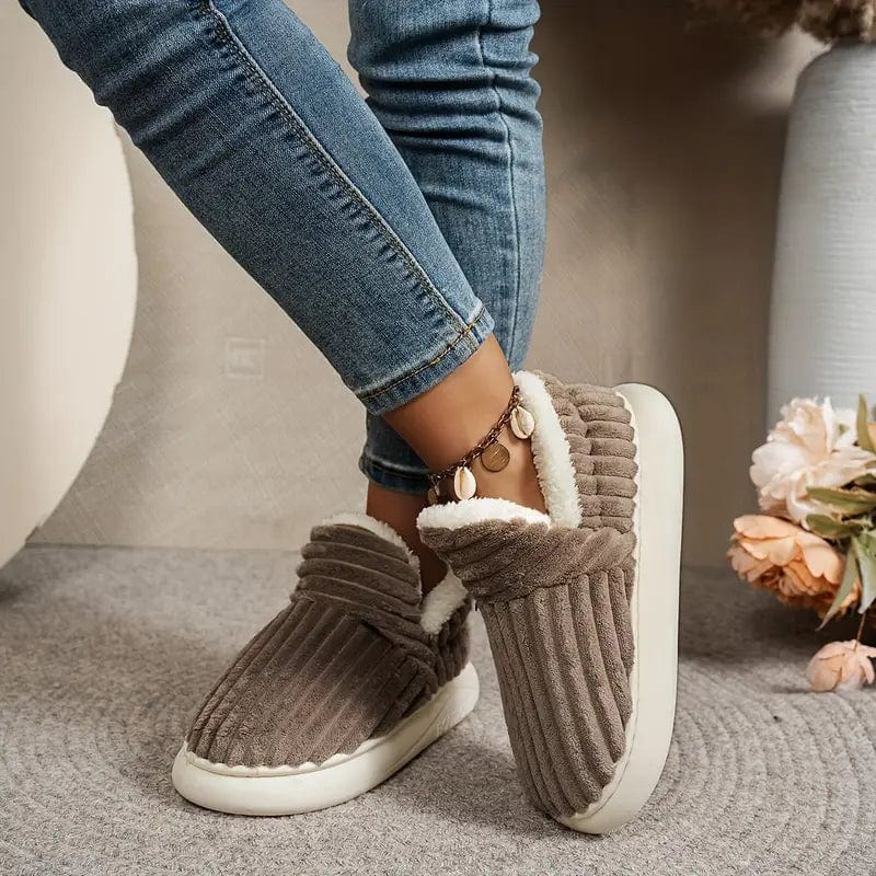 Damen tragen braune, plüschige Hausschuhe mit weißem Futter, kombiniert mit blauen Jeans. Bequeme, warme Slipper für den Winter.