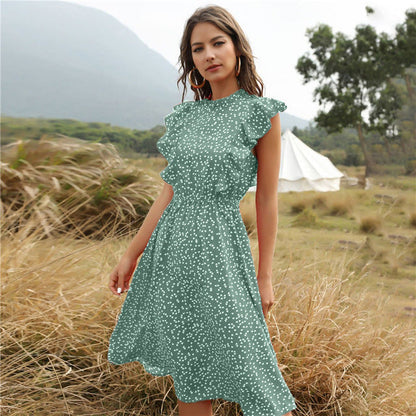 Frau in grünem, gepunktetem Kleid steht in natürlicher Landschaft mit Zelt im Hintergrund. Sommermode, Outdoor, Freizeitkleidung.