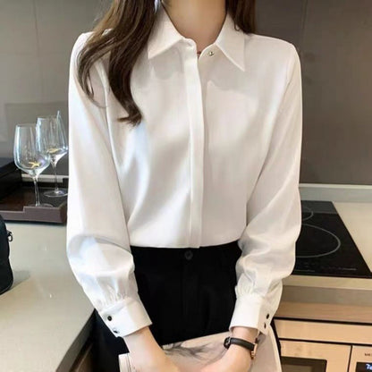 Frau in eleganter weißer Bluse und schwarzer Hose in moderner Küche, Weingläser im Hintergrund. Businessmode, Damenbekleidung, stilvoll.