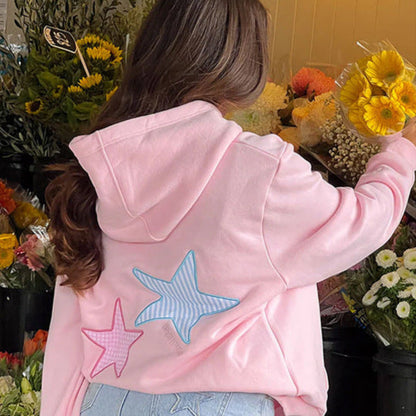 Frau in rosa Kapuzenpullover mit Seestern-Design, steht vor Blumenladen. Mode, Freizeitkleidung, Blumen, Kapuzenpullover, Seestern.