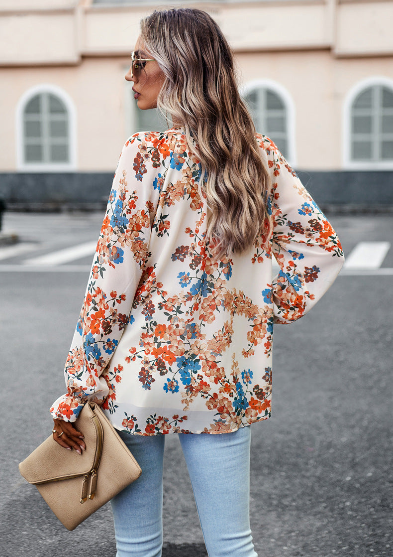 Frau mit blumiger Bluse und blonder, welliger Frisur, hält beigefarbene Clutch. Modetrend, Straßenstil, Frühlingsmode.
