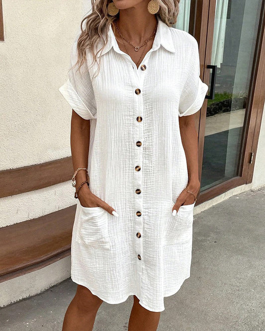 Frau in weißem Leinenhemdkleid mit Knopfleiste und Taschen, Sommermode, lässiger Stil, draußen stehend, modische Ohrringe und Armbänder.