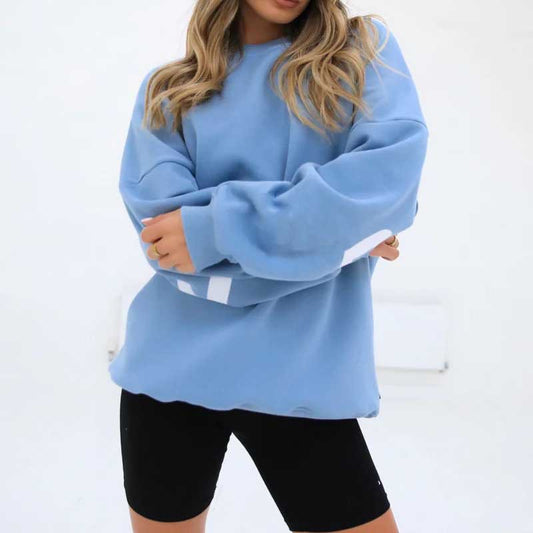 Frau in blauem Oversize-Pullover und schwarzen Radlerhosen vor weißem Hintergrund. Modetrend, lässiger Stil, bequeme Freizeitkleidung.