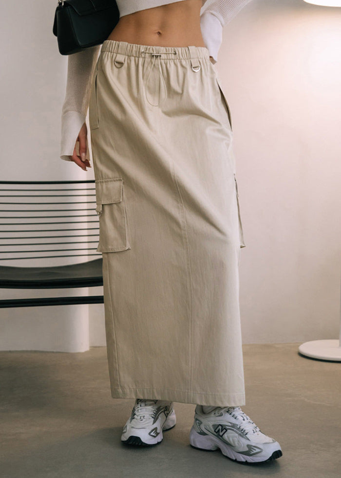 Beigefarbener Cargo-Rock mit Taschen, kombiniert mit weißen Sneakers und einem weißen Oberteil. Moderner Streetstyle-Look für Damenmode.