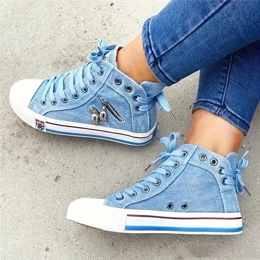 Blaue Jeans-Sneaker mit weißen Sohlen und dekorativen Reißverschlüssen, getragen von einer Person in blauen Jeans. Modische Freizeitschuhe.