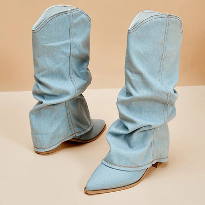 Hellblaue Denim-Stiefel mit spitzer Zehenpartie und niedrigen Absätzen auf beigem Hintergrund. Modische Damenstiefel, trendige Jeans-Optik.