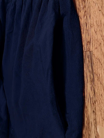 Dunkelblaues, strukturiertes Kleidungsstück aus Stoff, hängt an einer Holzwand. Mode, Textil, Kleidung, Stoffstruktur, Innenraum.