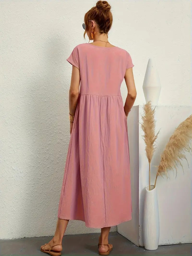 Frau in rosa Sommerkleid, steht mit dem Rücken zur Kamera, neben einer weißen Vase mit Pampasgras, minimalistische Einrichtung, lässiger Stil.