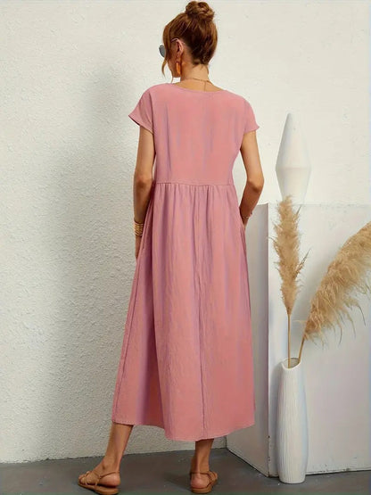 Frau in rosa Sommerkleid, steht mit dem Rücken zur Kamera, neben einer weißen Vase mit Pampasgras, minimalistische Einrichtung, lässiger Stil.