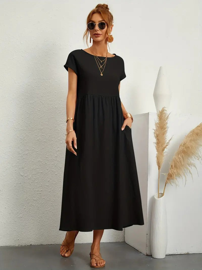 Frau in schwarzem Maxikleid mit kurzen Ärmeln, Sonnenbrille und Sandalen, steht neben Vase mit Pampasgras. Elegantes Sommeroutfit, lässiger Stil.