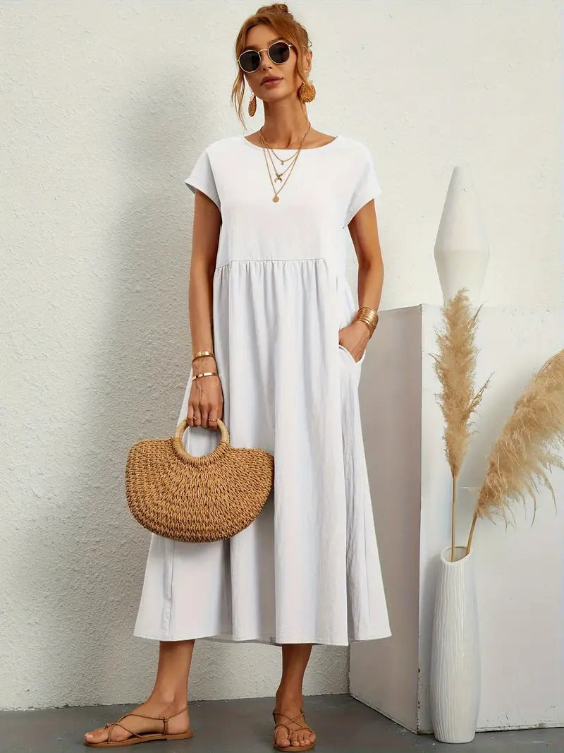 Frau in weißem Sommerkleid mit Strohtasche, Sonnenbrille und Sandalen vor weißer Wand. Mode, Sommeroutfit, Damenbekleidung, lässiger Stil.