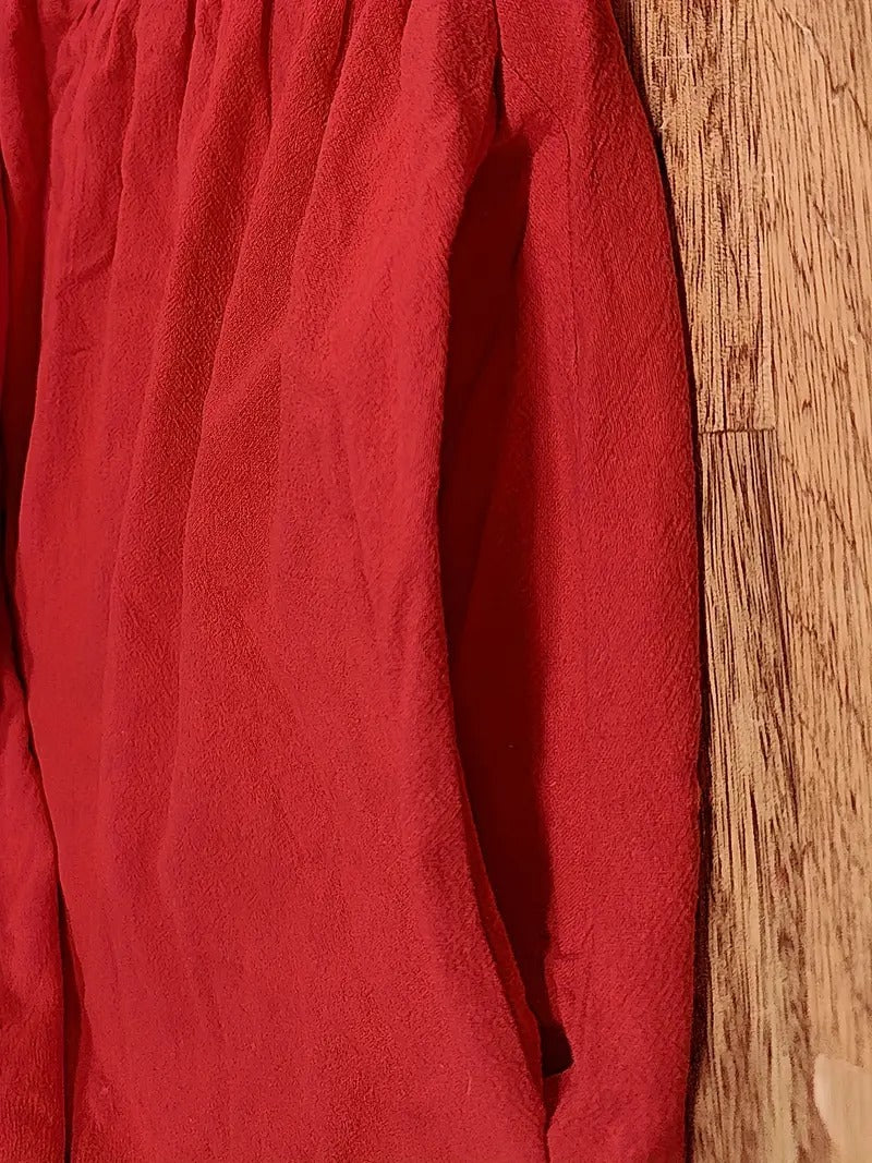 Rote Bluse aus leichtem Stoff, hängend an Holzwand. Modetrend, Damenbekleidung, elegante Oberbekleidung, stilvolle rote Bluse.