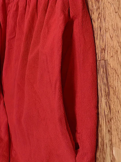 Rote Bluse aus leichtem Stoff, hängend an Holzwand. Modetrend, Damenbekleidung, elegante Oberbekleidung, stilvolle rote Bluse.