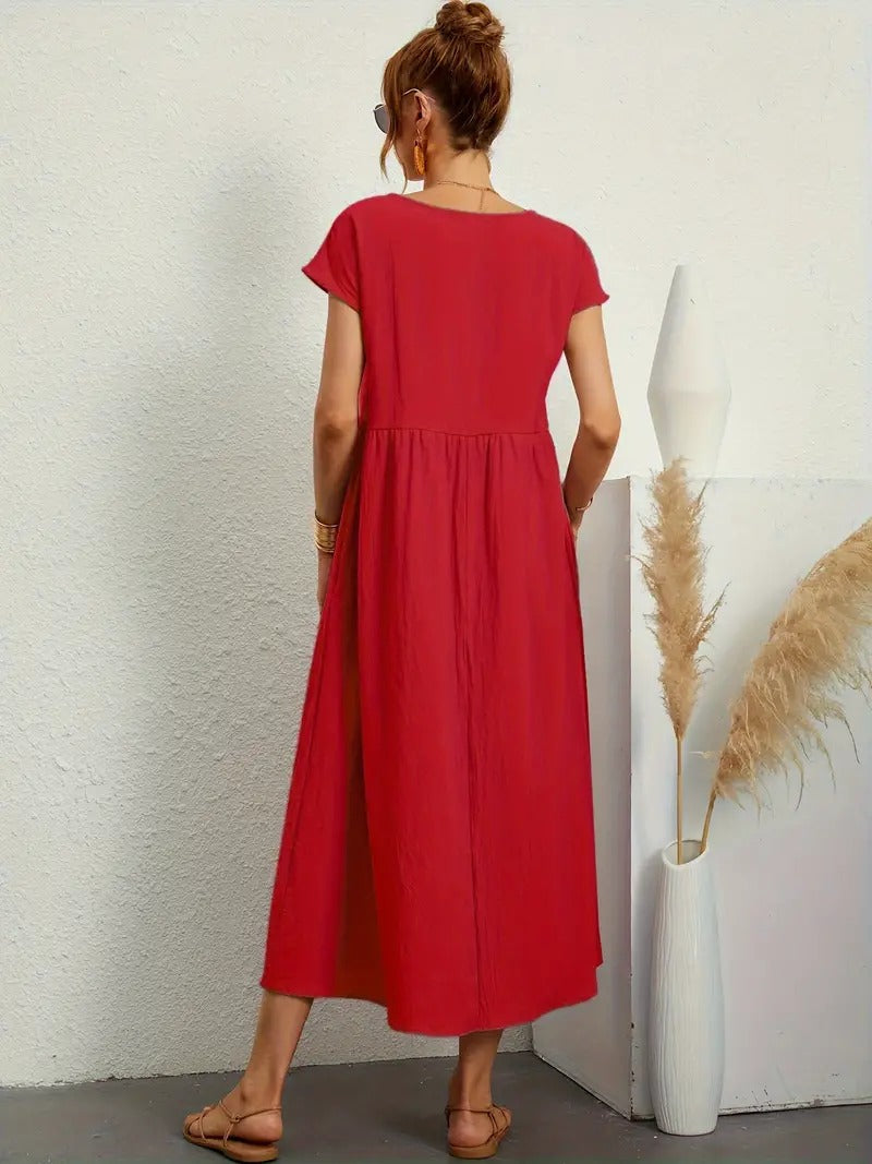 Frau in rotem Sommerkleid, steht mit dem Rücken zur Kamera. Neben ihr eine weiße Vase mit Pampasgras. Elegante, lässige Mode für den Sommer.
