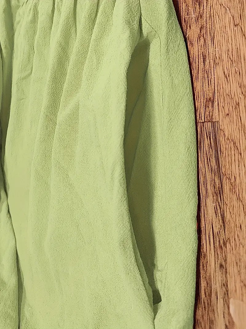 Grünes, zerknittertes Hemd auf Holzboden, Nahaufnahme. Mode, Textil, Kleidung, Stoffstruktur, Falten, Holzoberfläche.