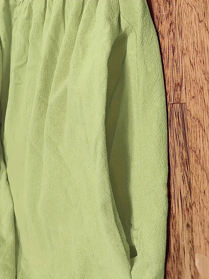 Grünes, zerknittertes Hemd auf Holzboden, Nahaufnahme. Mode, Textil, Kleidung, Stoffstruktur, Falten, Holzoberfläche.