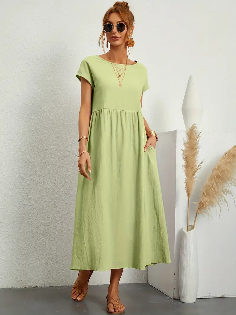 Frau in grünem Sommerkleid, trägt Sonnenbrille und Sandalen, steht neben Vase mit Pampasgras. Modetrend, lässiger Stil, Sommermode.
