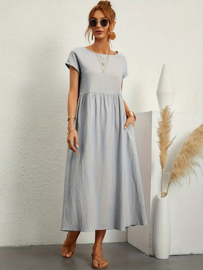 Frau in grauem Sommerkleid, trägt Sonnenbrille und Schmuck, steht neben Vase mit Pampasgras. Modetrend, lässiger Stil, Sommermode 2023.