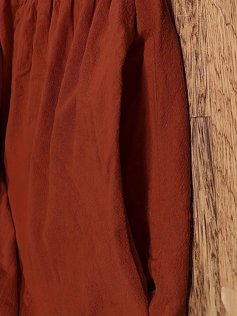 Rotes, langärmeliges Hemd aus Leinenstoff, hängend an einer Holzwand. Textur und Falten des Stoffes sichtbar. Mode, Kleidung, Textildesign.