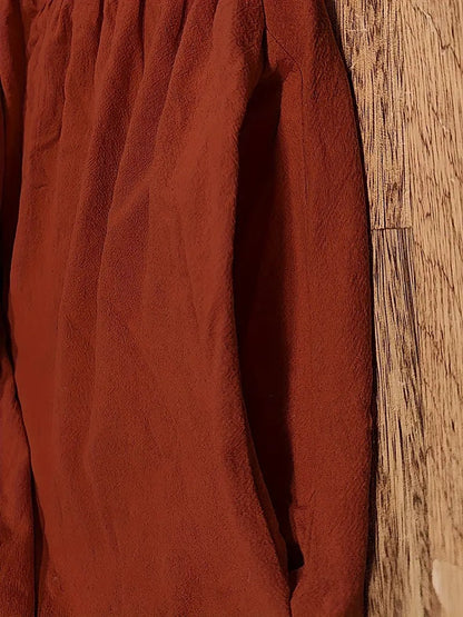 Rotes, langärmeliges Hemd aus Leinenstoff, hängend an einer Holzwand. Textur und Falten des Stoffes sichtbar. Mode, Kleidung, Textildesign.