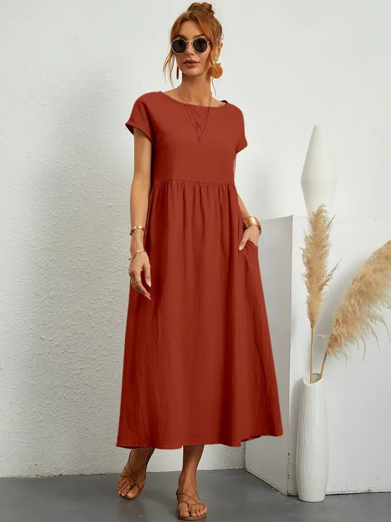 Frau in rotem Maxikleid, Sonnenbrille und Sandalen, steht neben weißer Vase mit Pampasgras. Elegante Sommermode, lässiger Look.
