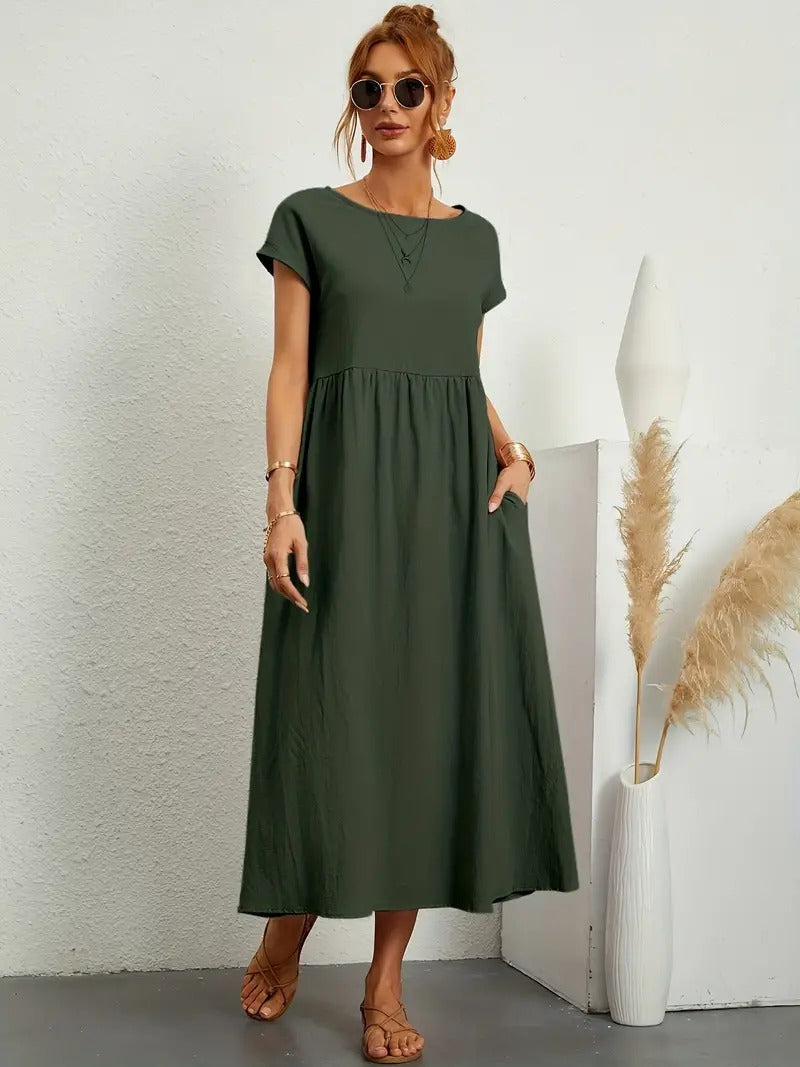 Frau in grünem Maxikleid, Sonnenbrille und Sandalen, steht neben Vase mit Pampasgras. Sommermode, lässiger Stil, minimalistisches Design.