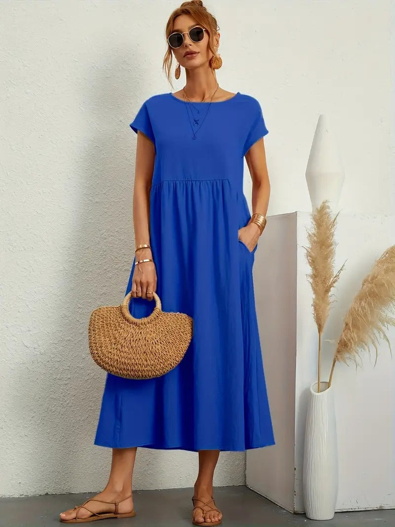 Frau in blauem Sommerkleid mit Strohtasche, Sonnenbrille und Sandalen vor weißer Wand. Mode, Damenbekleidung, Sommeroutfit, lässiger Stil.