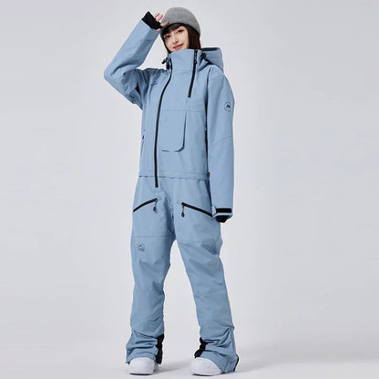 Frau in hellblauem Skianzug mit Kapuze und grauer Mütze, steht aufrecht. Wintermode, Outdoor-Bekleidung, Skibekleidung für Damen.