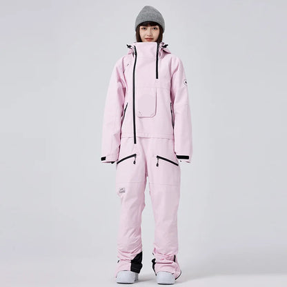 Frau in rosa Skianzug mit Kapuze und grauer Mütze, isoliert vor grauem Hintergrund. Wintermode, Skibekleidung, Outdoor-Ausrüstung.