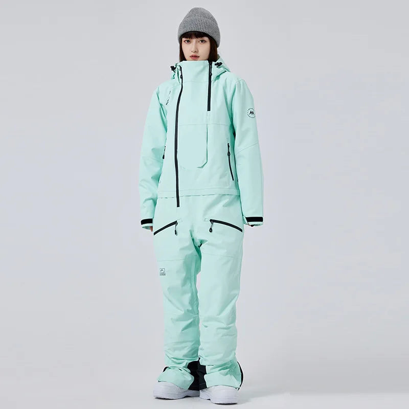 Frau in mintgrünem Skianzug mit Kapuze und grauer Mütze, isolierter Hintergrund. Wintermode, Skibekleidung, Outdoor-Ausrüstung.