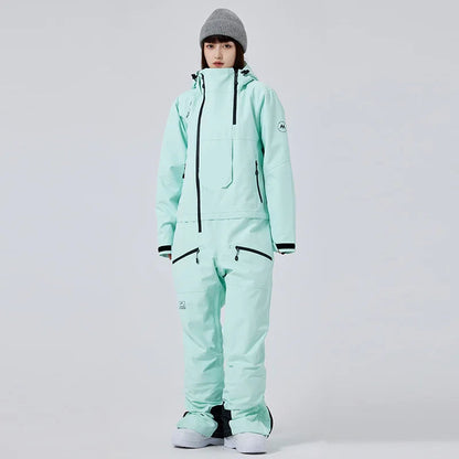 Frau in mintgrünem Skianzug mit Kapuze und grauer Mütze, isolierter Hintergrund. Wintermode, Skibekleidung, Outdoor-Ausrüstung.