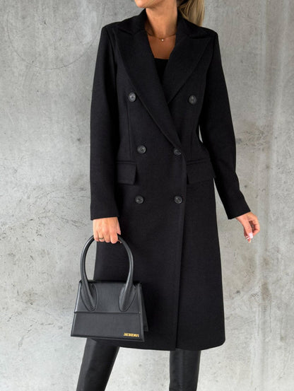 Eleganter schwarzer Damenmantel, doppelreihig, kombiniert mit schwarzer Handtasche und Stiefeln, vor grauem Hintergrund. Fashion, Herbstmode.