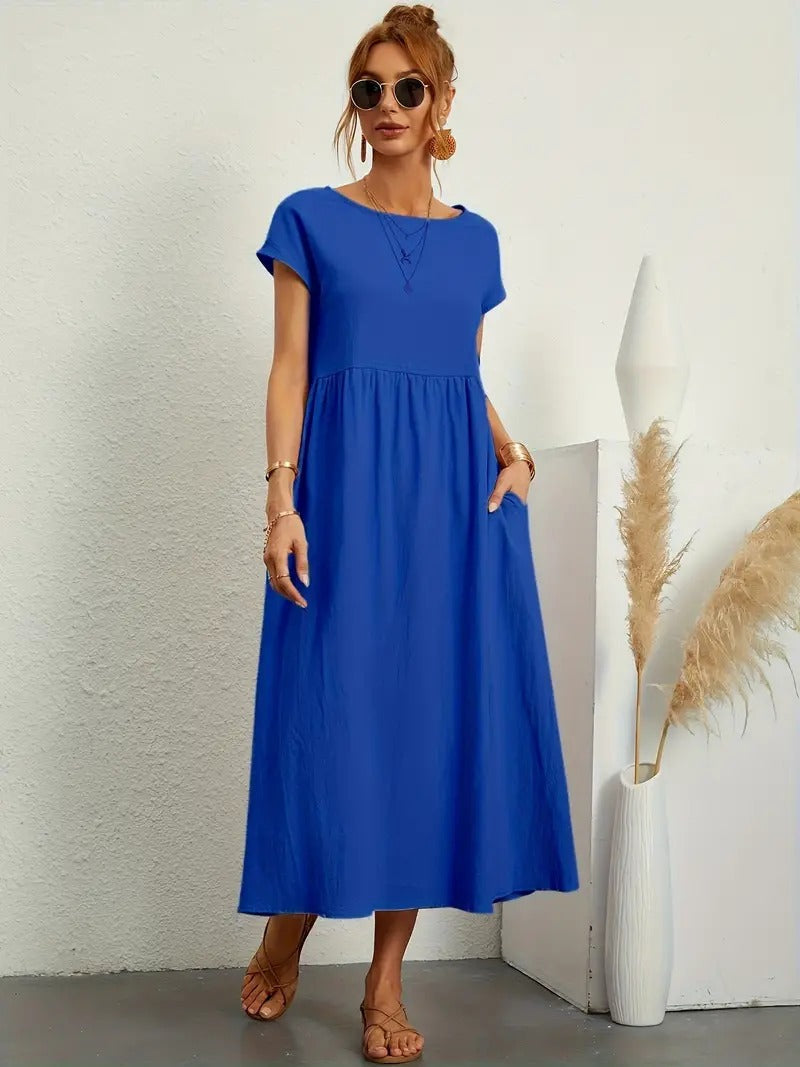 Frau in blauem Sommerkleid, Sonnenbrille, Sandalen, steht neben Vase mit Pampasgras. Modetrend, lässiger Stil, Sommermode 2023.