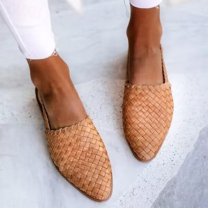 Braune, geflochtene Lederslipper an Frauenfüßen auf hellem Steinboden, modische Sommerschuhe, lässiger Stil, Nahaufnahme.