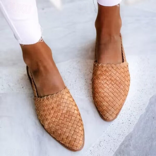 Braune, geflochtene Lederslipper an Frauenfüßen auf hellem Steinboden, modische Sommerschuhe, lässiger Stil, Nahaufnahme.