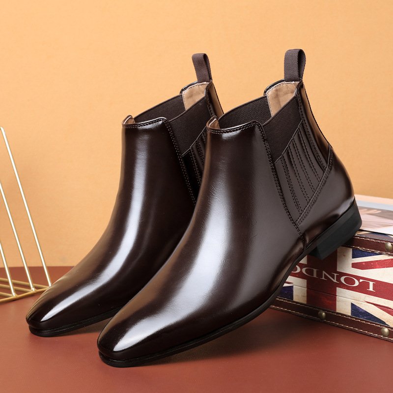 Elegante braune Chelsea Boots aus Leder, glänzend poliert, auf einem Tisch mit britischer Flagge im Hintergrund. Ideal für Herrenmode und Business-Look.