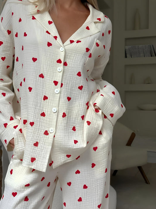 Frau in weißem Pyjama mit roten Herzmustern, gemütliches Schlafzimmer, moderne Einrichtung, Nachtwäsche, entspannte Atmosphäre.