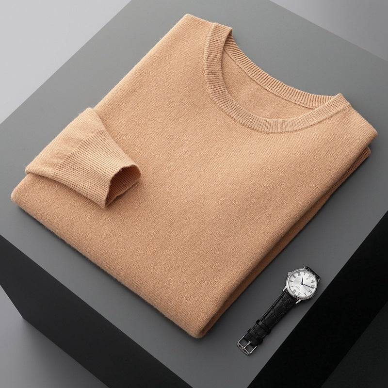 Beigefarbener Pullover aus Kaschmir, sorgfältig gefaltet auf grauem Tisch, neben einer eleganten Armbanduhr mit schwarzem Lederarmband und silbernem Zifferblatt.