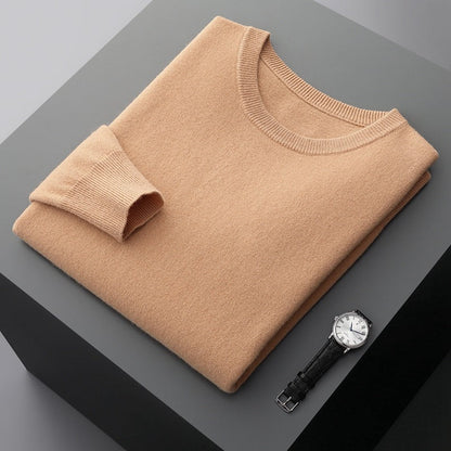 Beigefarbener Pullover aus Kaschmir, sorgfältig gefaltet auf grauem Tisch, neben einer eleganten Armbanduhr mit schwarzem Lederarmband und silbernem Zifferblatt.