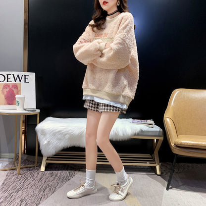 Frau in beigem Teddy-Pullover und karierter Shorts posiert in modernem Wohnzimmer. Modetrend, gemütlicher Look, Herbstmode, stilvolle Kleidung.