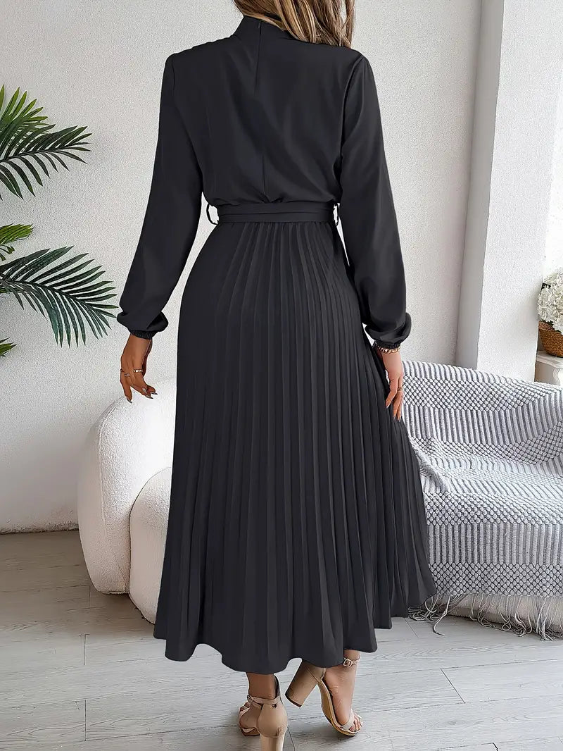Frau in elegantem, schwarzem, langem Plisseekleid, steht in modernem Wohnzimmer mit Pflanzen und Sofa, stilvolle Mode, Rückansicht.
