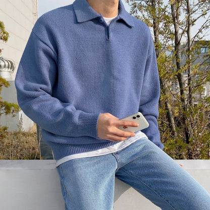Blauer Strickpullover, lässig getragen von Person mit Smartphone, kombiniert mit Jeans. Perfekt für Herbstmode und Freizeitoutfits im Freien.