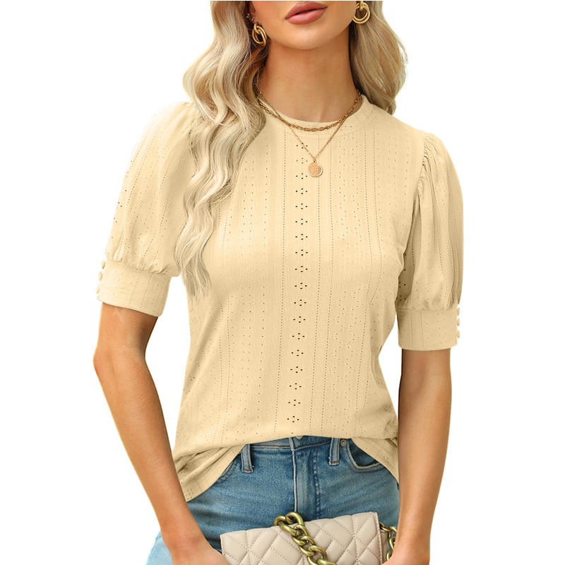 Frau in beiger, kurzärmeliger Bluse mit Lochmuster, trägt goldene Halsketten und blaue Jeans, hält gesteppte Handtasche. Elegante Damenmode.