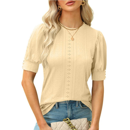 Frau in beiger, kurzärmeliger Bluse mit Lochmuster, trägt goldene Halsketten und blaue Jeans, hält gesteppte Handtasche. Elegante Damenmode.