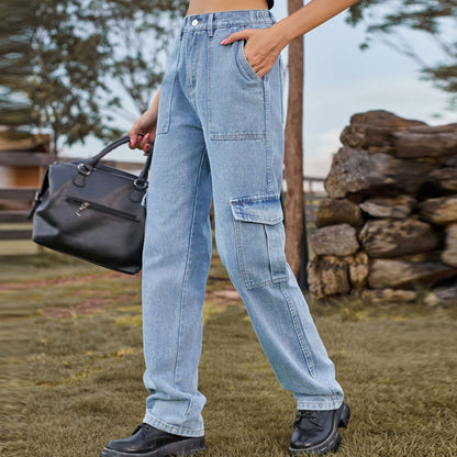 Frau in blauer Cargo-Jeans und schwarzen Stiefeln, hält schwarze Handtasche. Outdoor-Hintergrund mit Steinmauer. Modetrend, Freizeitlook.