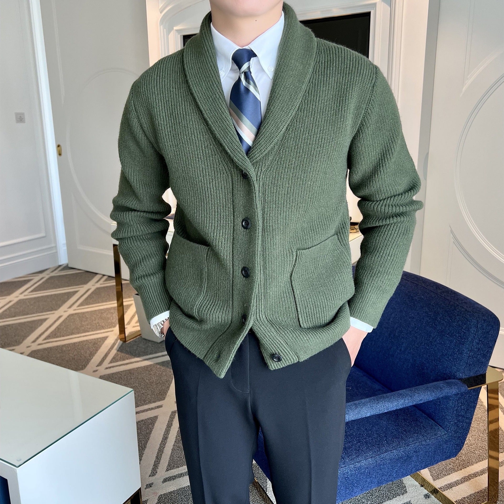Mann in grünem Strick-Cardigan mit Krawatte und schwarzer Hose in modernem Wohnzimmer. Elegante Herrenmode, stilvoller Look, modische Kleidung.