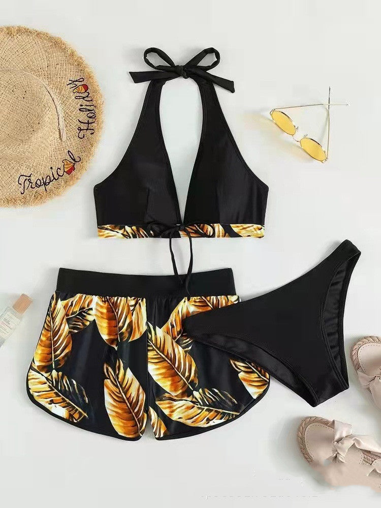 Schwarzer Bikini mit tropischem Blattmuster, Strohhut, Sonnenbrille und Sandalen auf hellem Hintergrund. Perfekt für Sommer und Strandurlaub.
