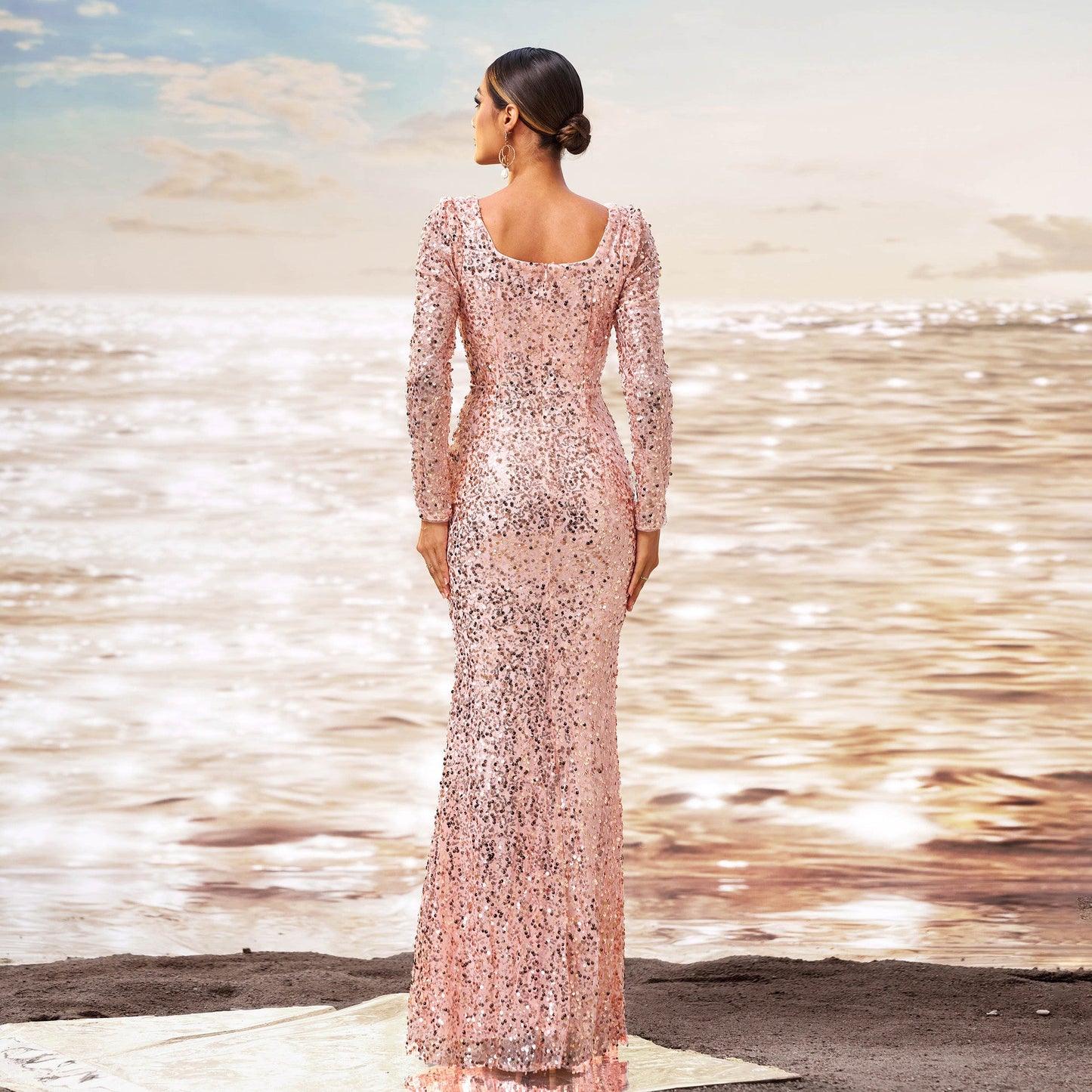 Frau in elegantem, rosa Paillettenkleid am Strand, Sonnenuntergang im Hintergrund, glamouröse Abendmode, stilvolle Strandkulisse.